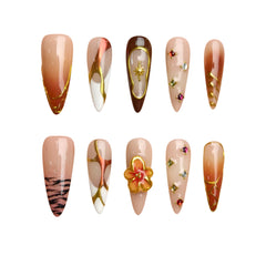 Long stiletto press-on nails in bronze with gold abstract lines and floral accents, perfect for bold fashion looks.
