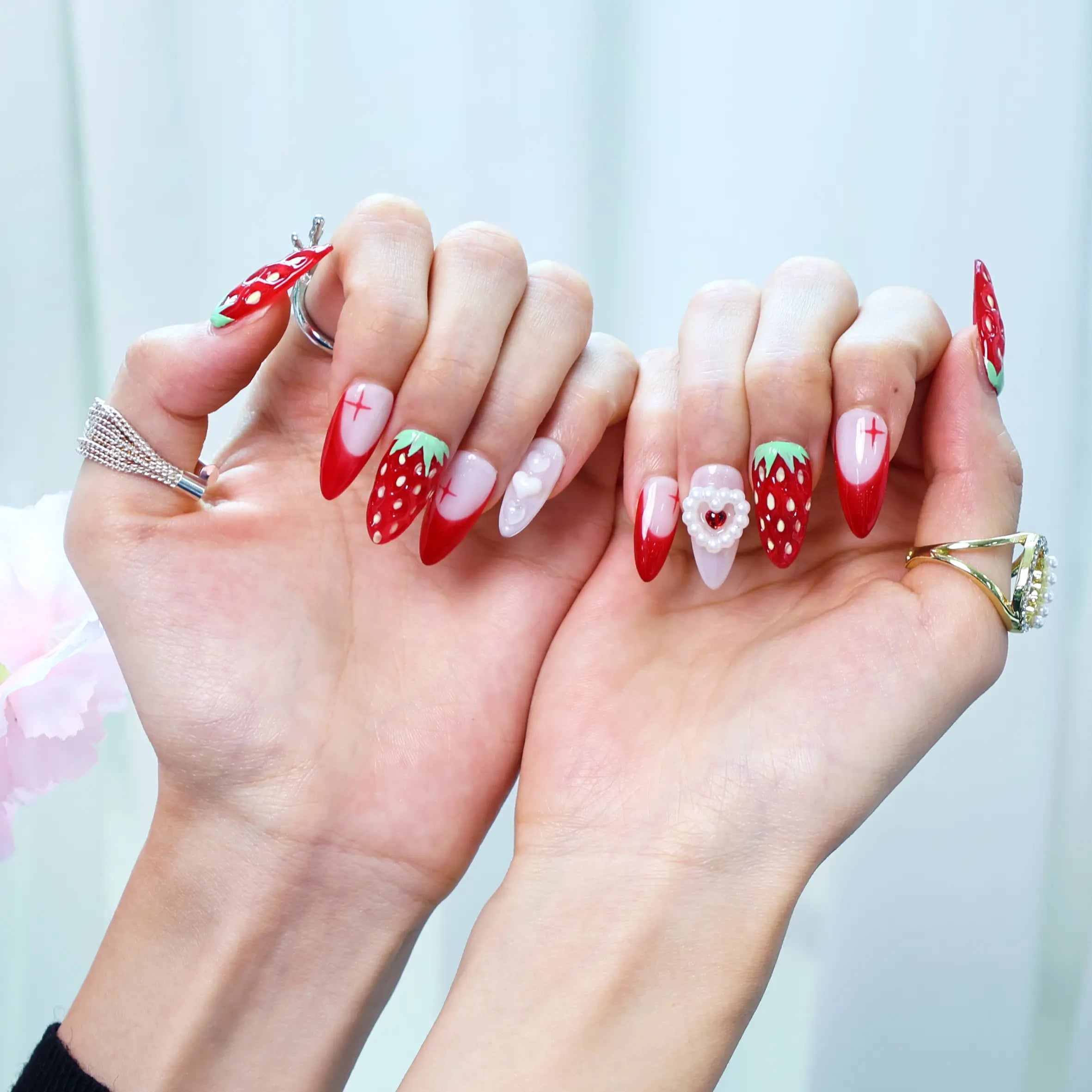 Hand pose showing vibrant red to white nails with fruity 3D design and soft-glam pearl touches