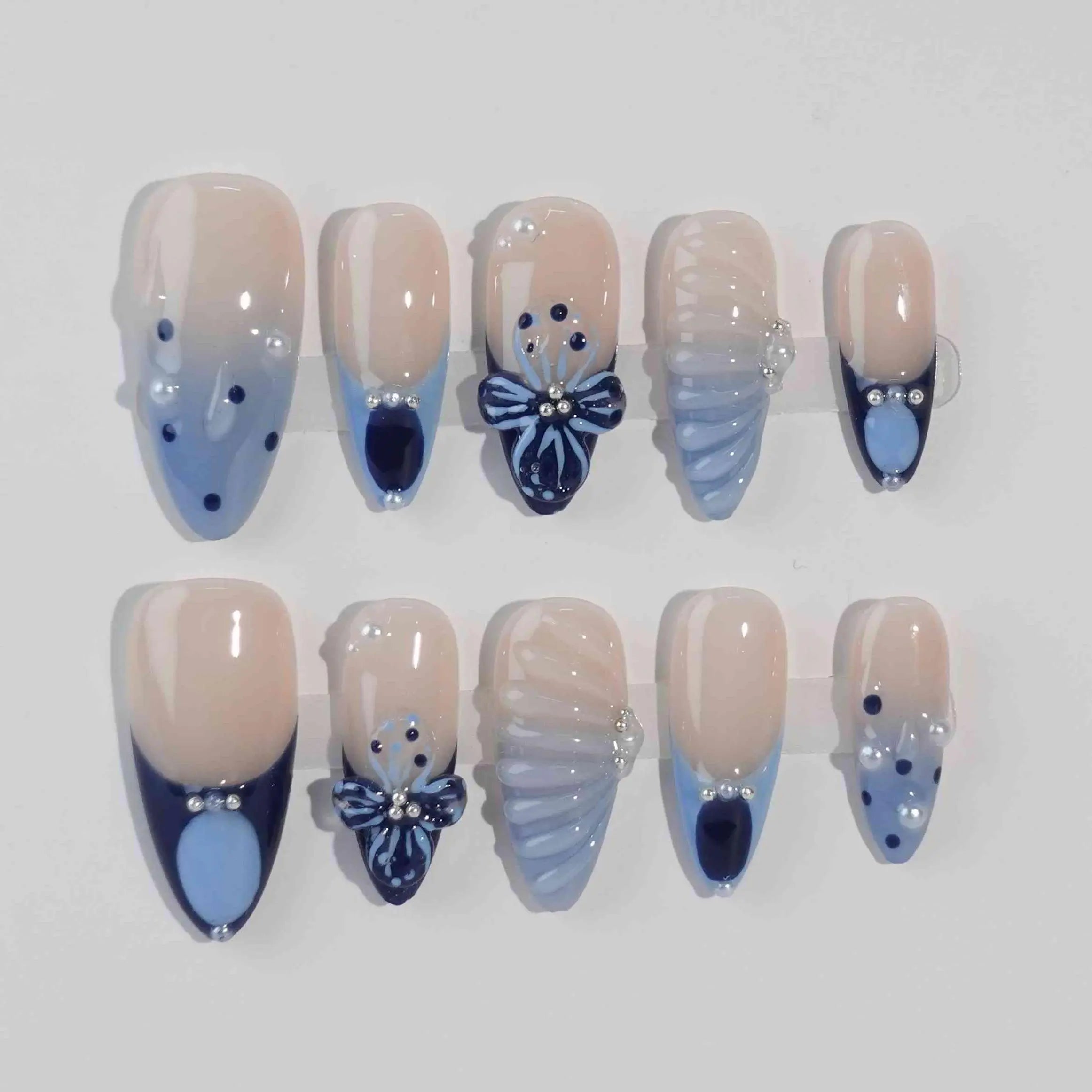 Handmade blue almond press-on nails featuring beige base, subtle 3D floral accents, and a soft French tip style.
