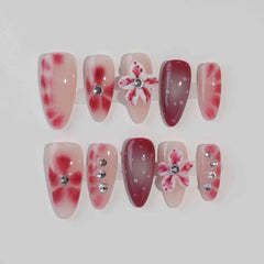 Medium almond press-on nails in pink and red gradient with 3D floral accents and rhinestones.