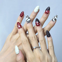 Hand model wearing medium almond nails in matte brown and white swirl design with cute 3D strawberry details