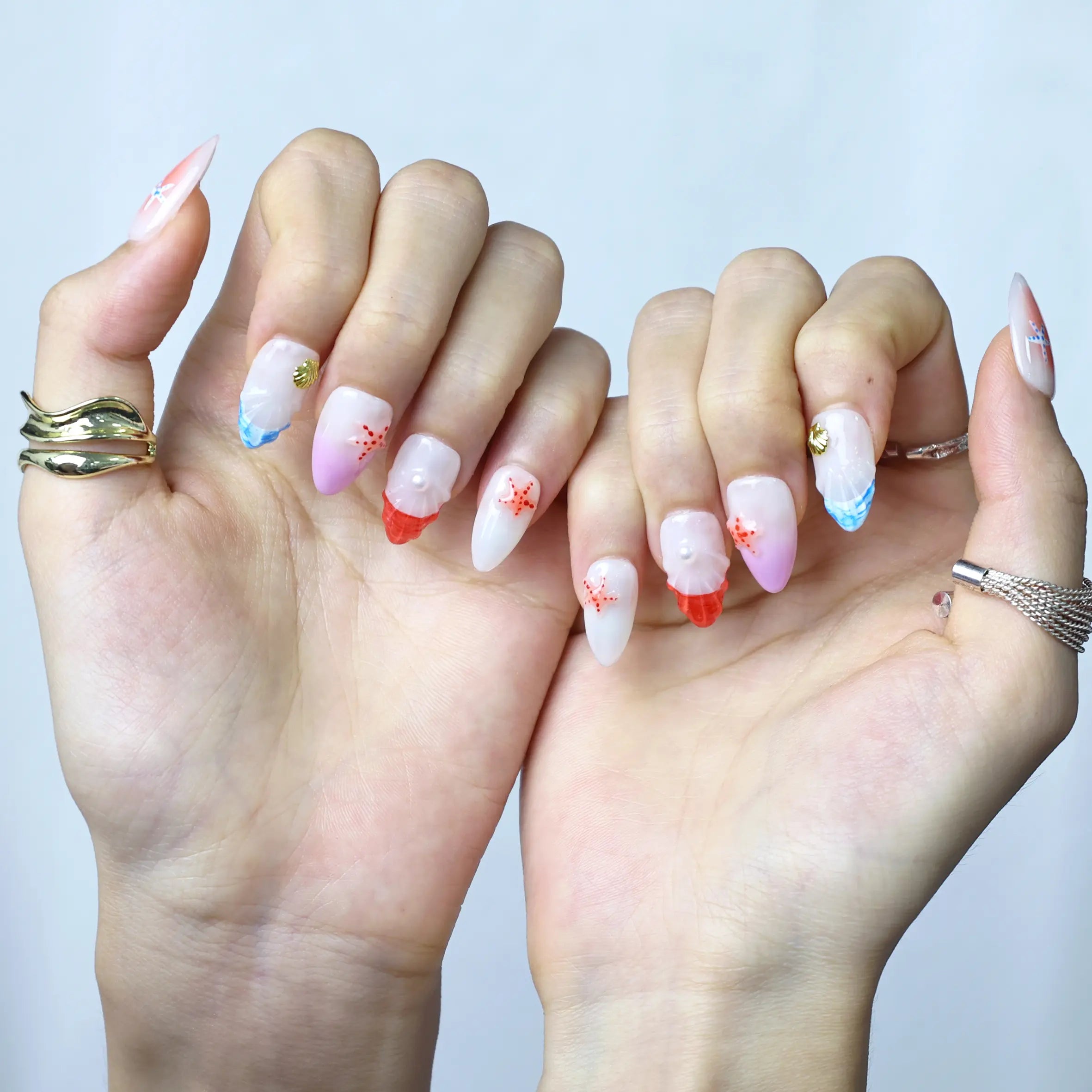 Hand model showing pink-to-coral gradient almond nails with tiny seashell embellishments