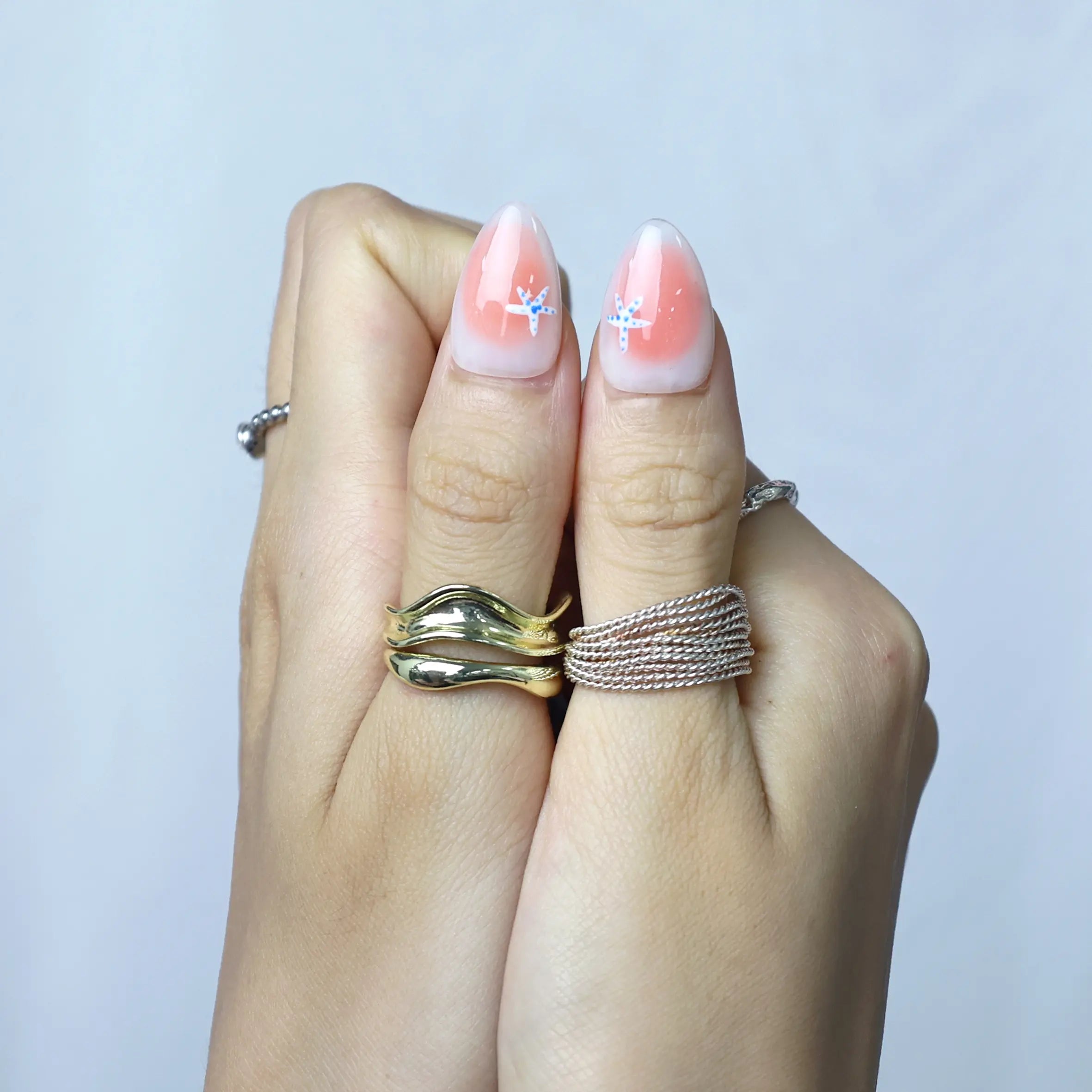 Press-on nails with coral tones and marine-inspired accents, styled on hand in natural light