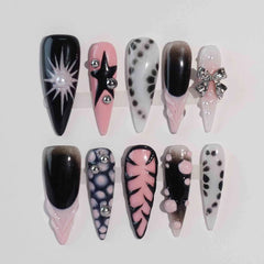 Long pink press on nails with black and grey ombre, rhinestones, and star accents – pointed for cosmic glam looks.