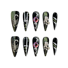 Long black stiletto press-on nails with green shimmer, 3D scorpions, crystal skulls, and eerie embellishments for a bold gothic statement
