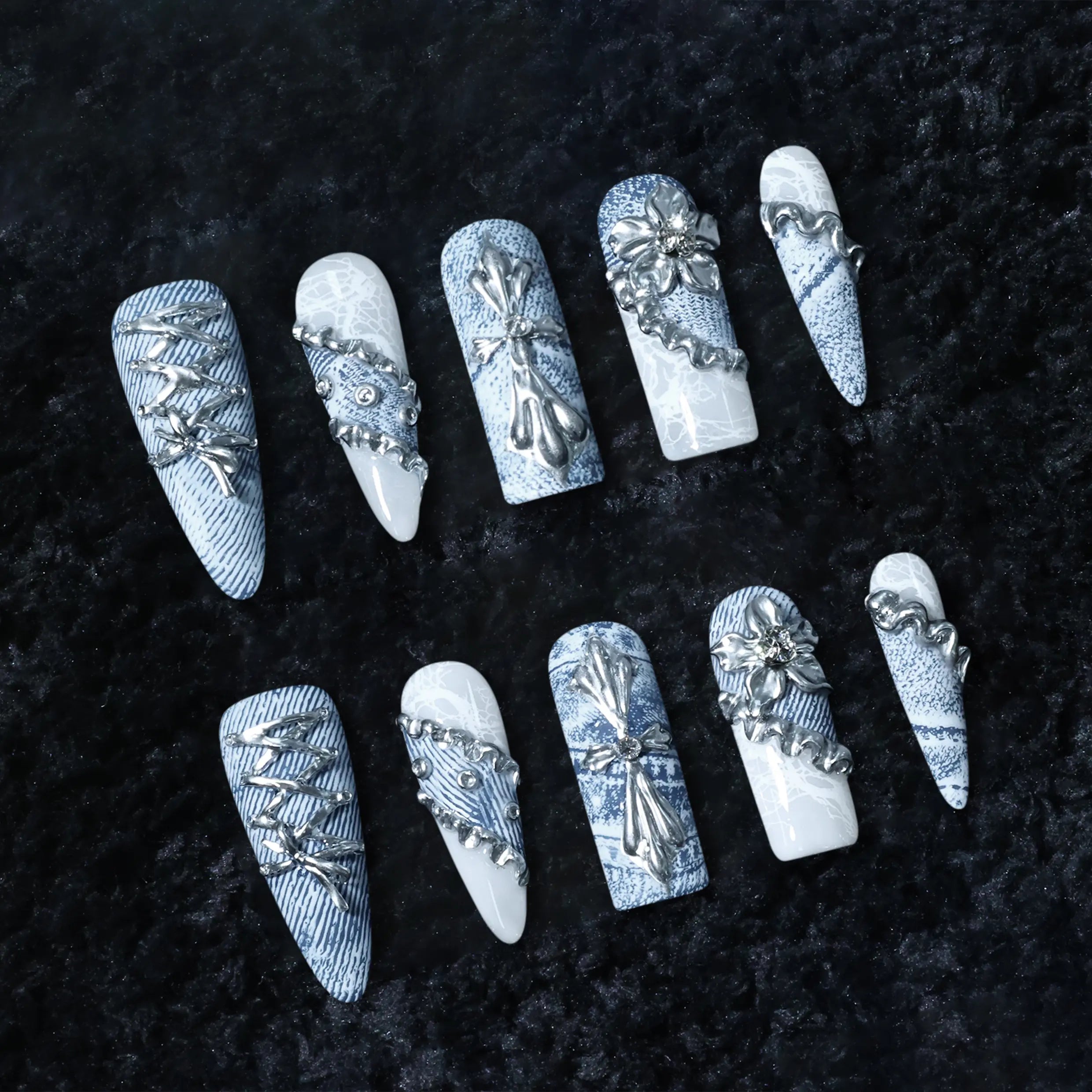 Blue denim-inspired stiletto-shaped press-on nails featuring white marble accents, metallic lace-up designs, and floral appliqués.