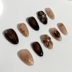 Almond press on nails with glossy caramel to espresso brown gradient and gold flake accents.