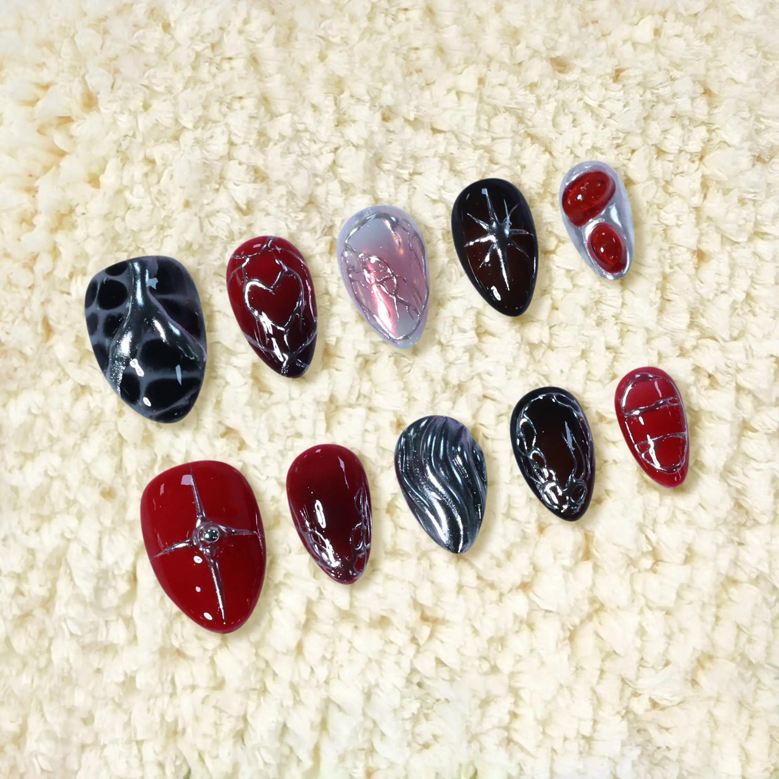 Fiery red and black short almond press-on nails with molten chrome, shattered-glass textures, and sculpted heart accents.