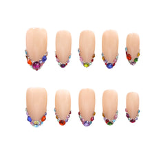 Almond press on nails with nude base and colorful rhinestone tips.