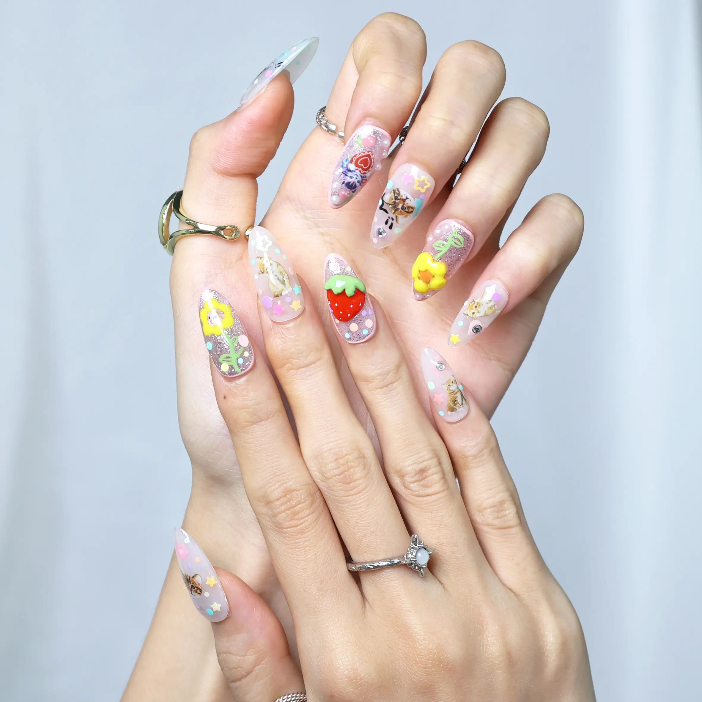 Close-up of glittery pink nails featuring kawaii character accents, strawberries, and layered flowers
