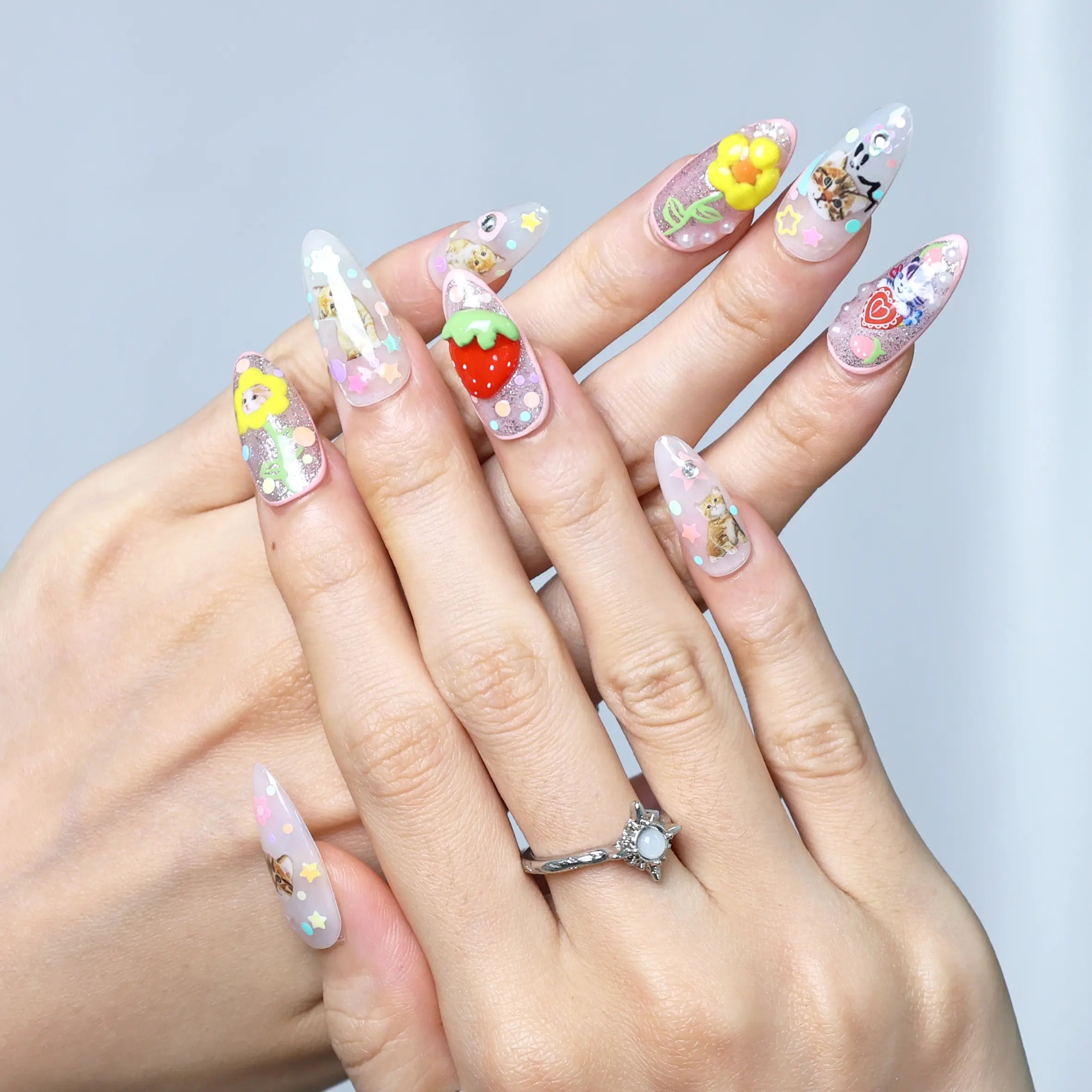 Side angle of almond-shaped nails with sparkling pink base, playful fruit motifs, and 3D cute characters