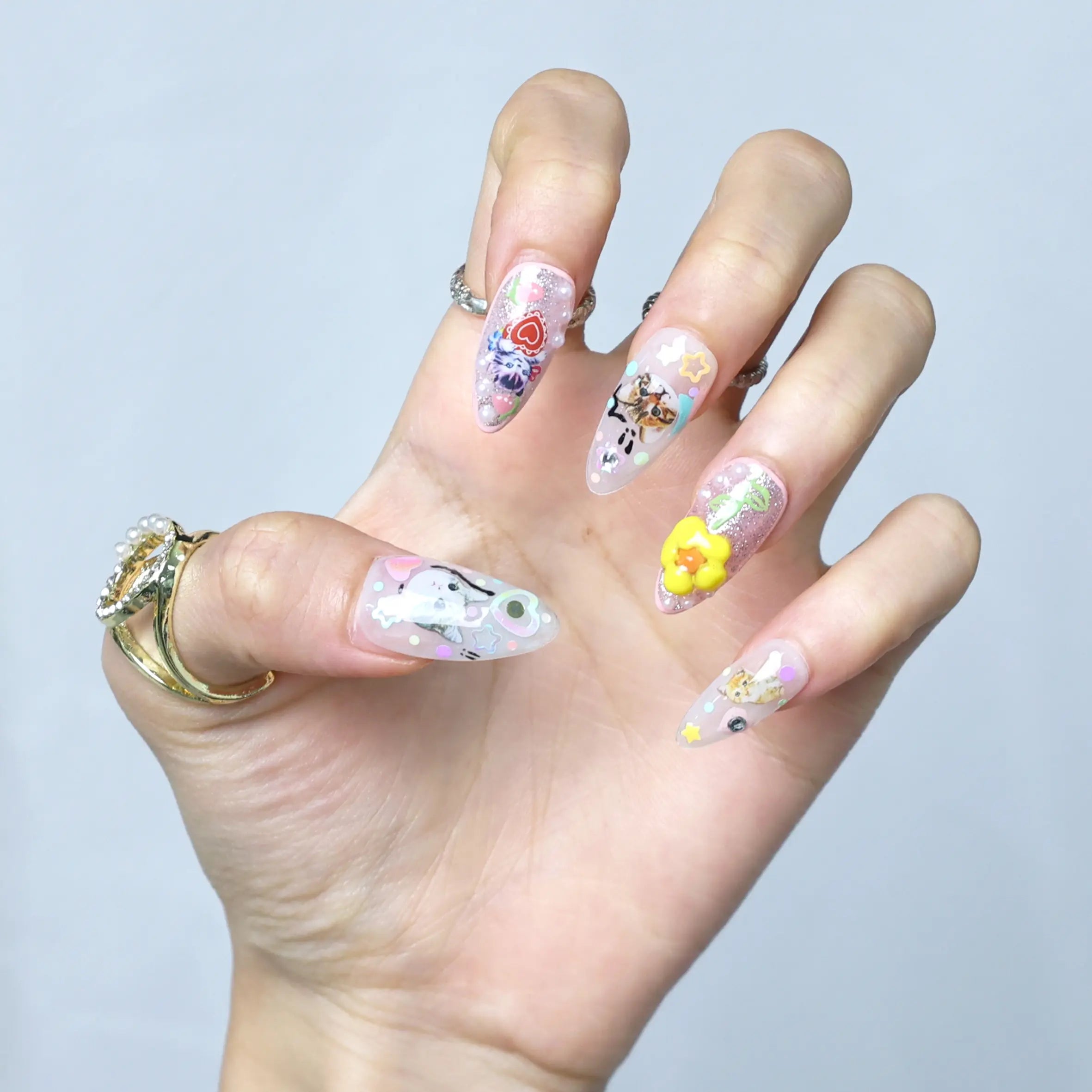 Hand pose highlighting vibrant pink nails with handcrafted kawaii figures, flower charms, and fruity sparkle