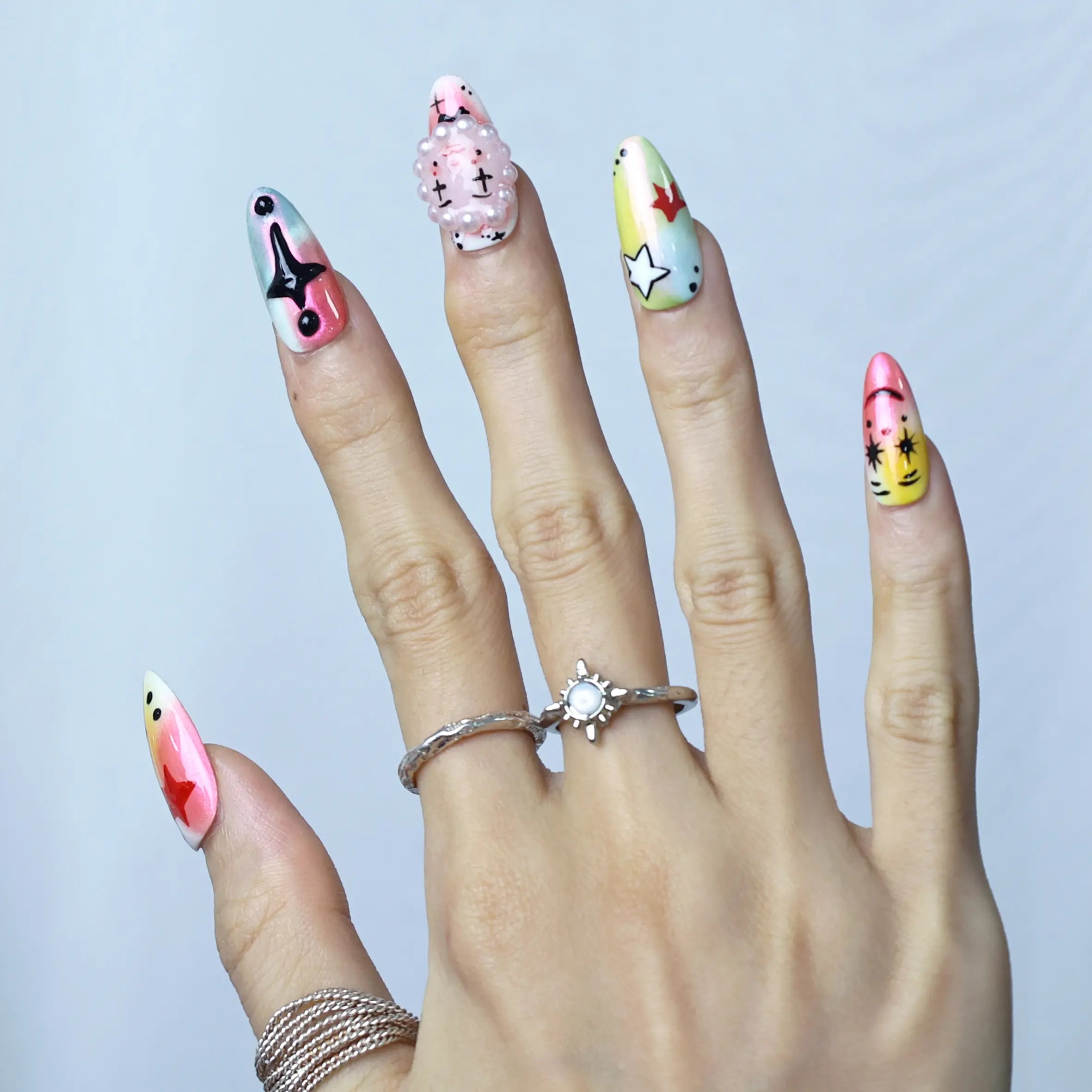 Hand model wearing medium almond nails with pastel pink base, 3D cartoon eyes, and playful clown-style accents