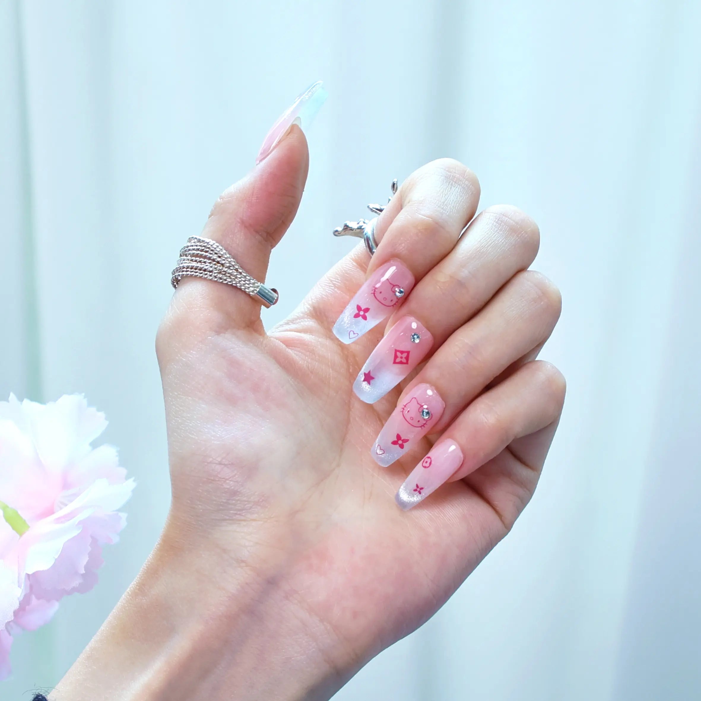 Close-up of press-on nails featuring pink base, glitter fade, and playful red bow accents