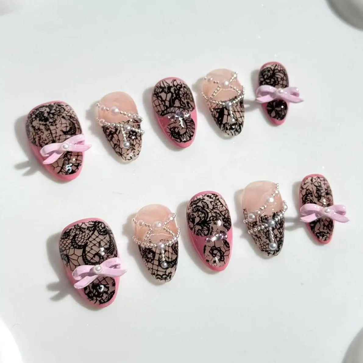 Medium almond press on nails with black lace detail and pink bow accents.