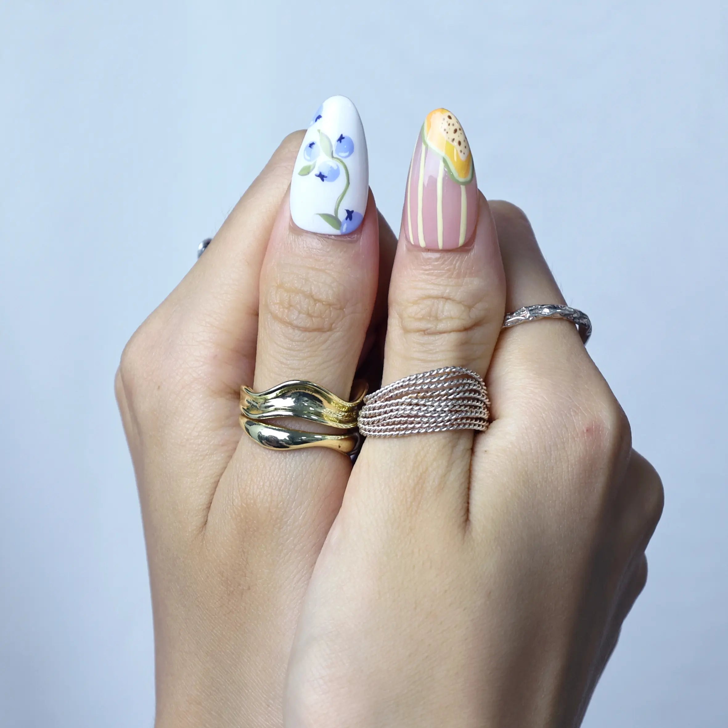 Hand model wearing medium almond nails in soft pink with hand-painted floral accents and tiny fruit charms