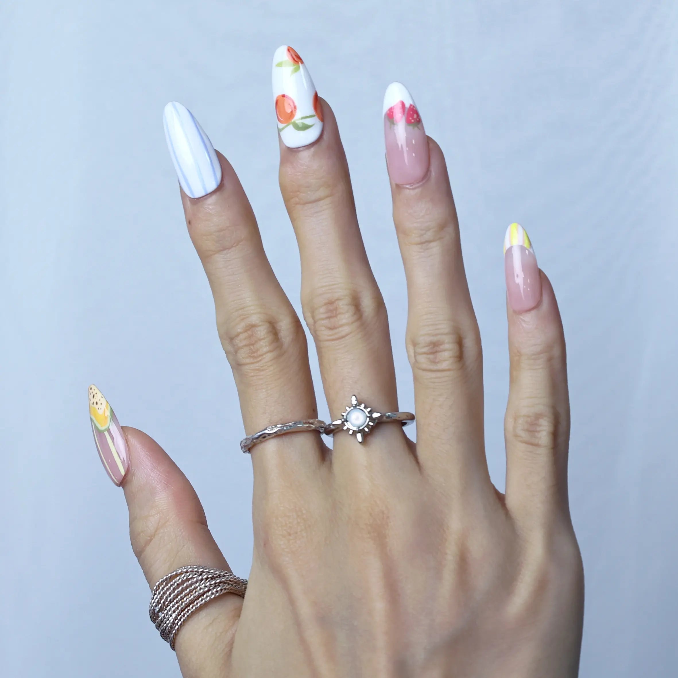 Side view of medium almond nails featuring pastel floral prints and small fruit details for a fresh summer look