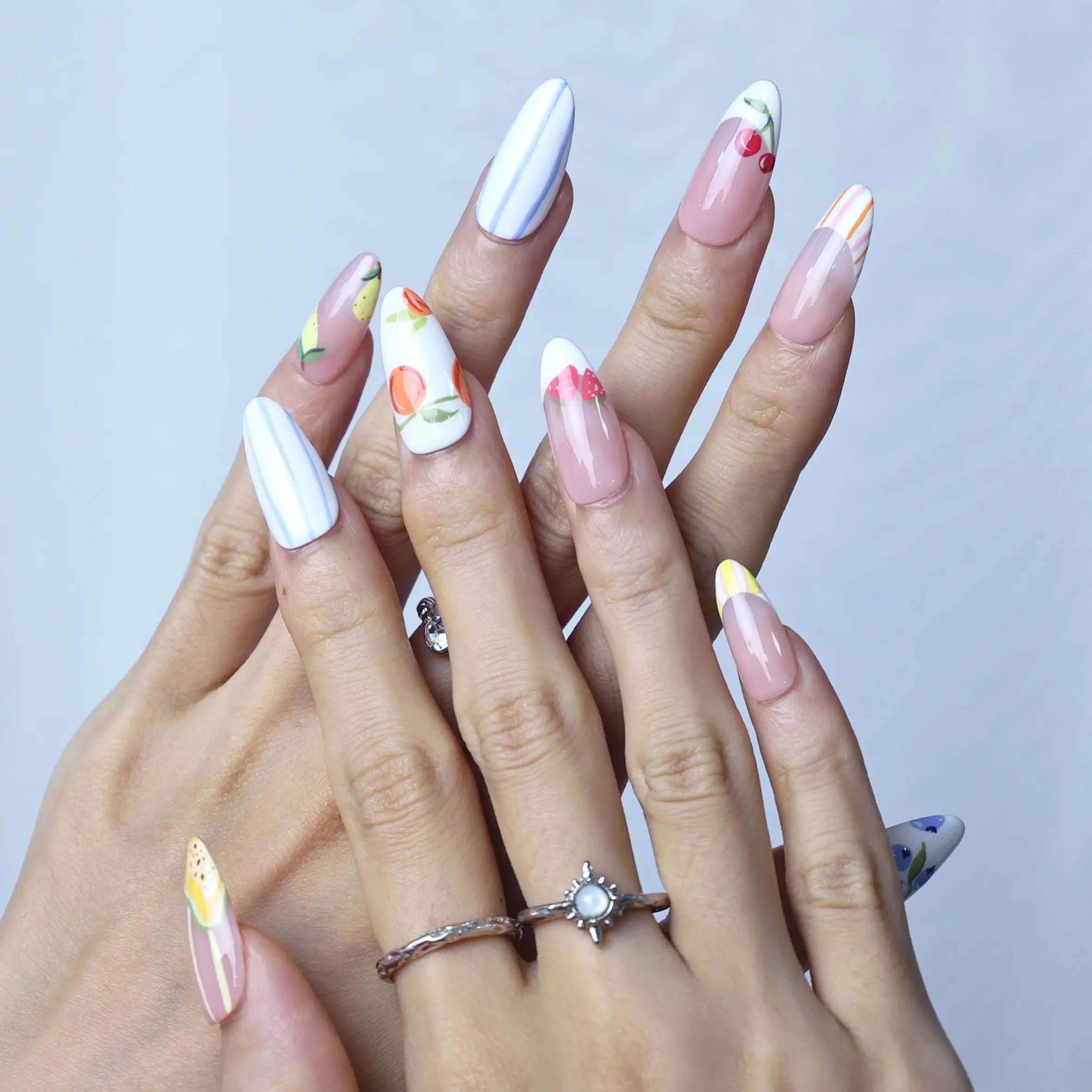 Feminine and playful nails with subtle pink tones, floral art, and fruit-themed accents perfect for spring/summer