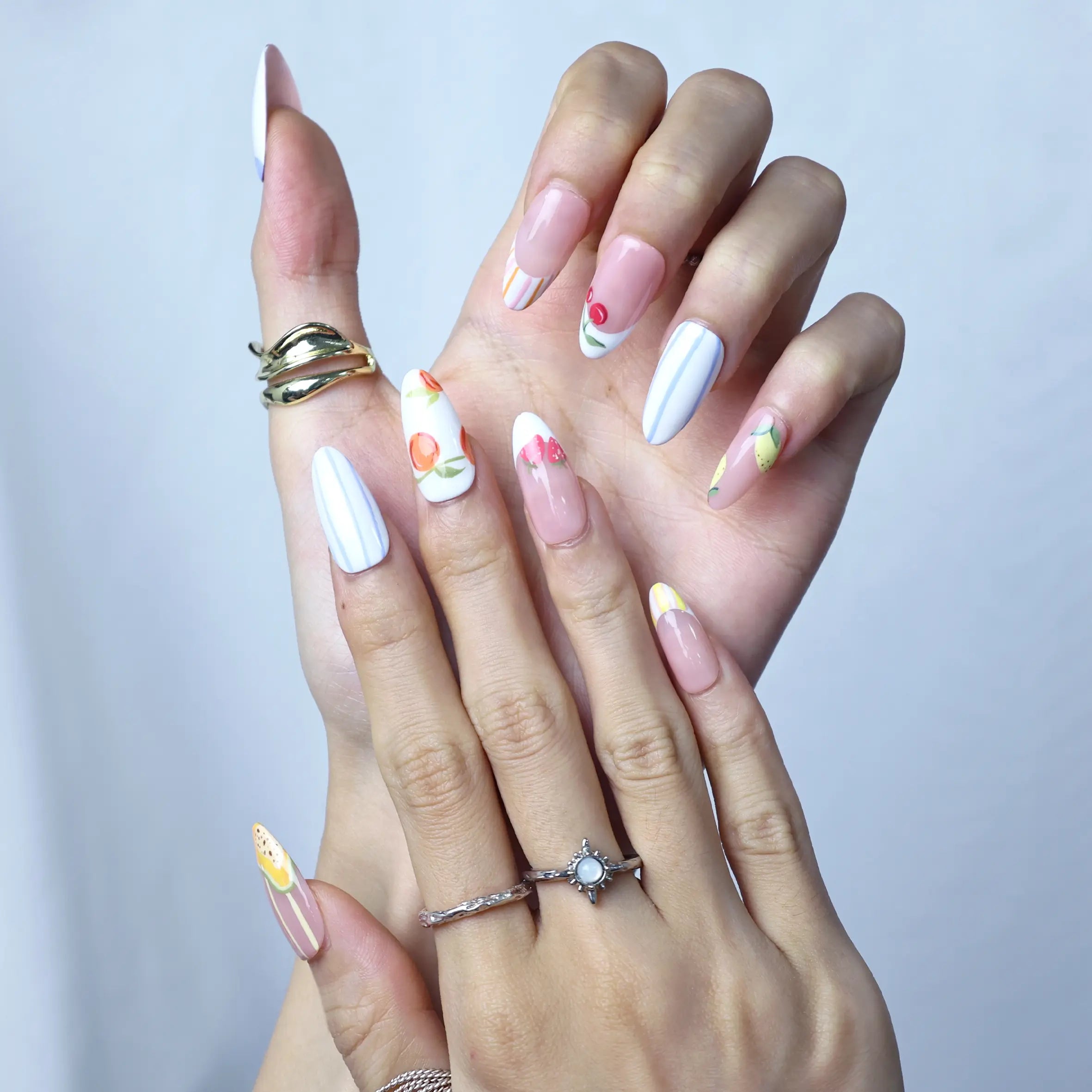Hand pose showing full set of press-on nails in soft pink with floral-fruit mix and natural glossy finish