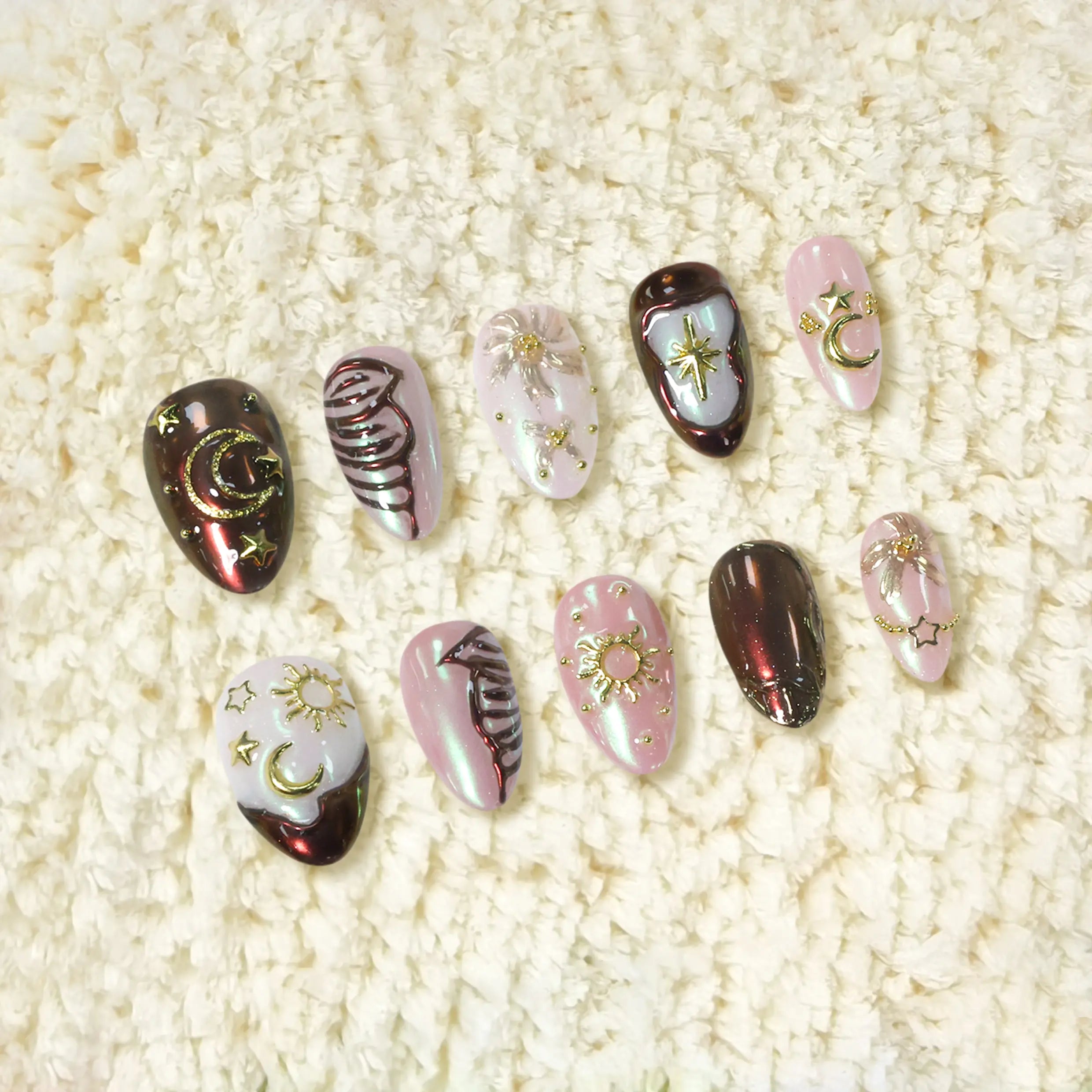 Handmade almond press-on nails in iridescent pink, brown, and white with gold moon, sun, and star charms for a cosmic-inspired design.