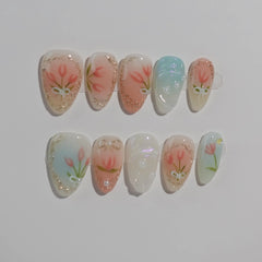 Almond press on nails in soft peach and mint with delicate floral art, ideal for spring and summer.