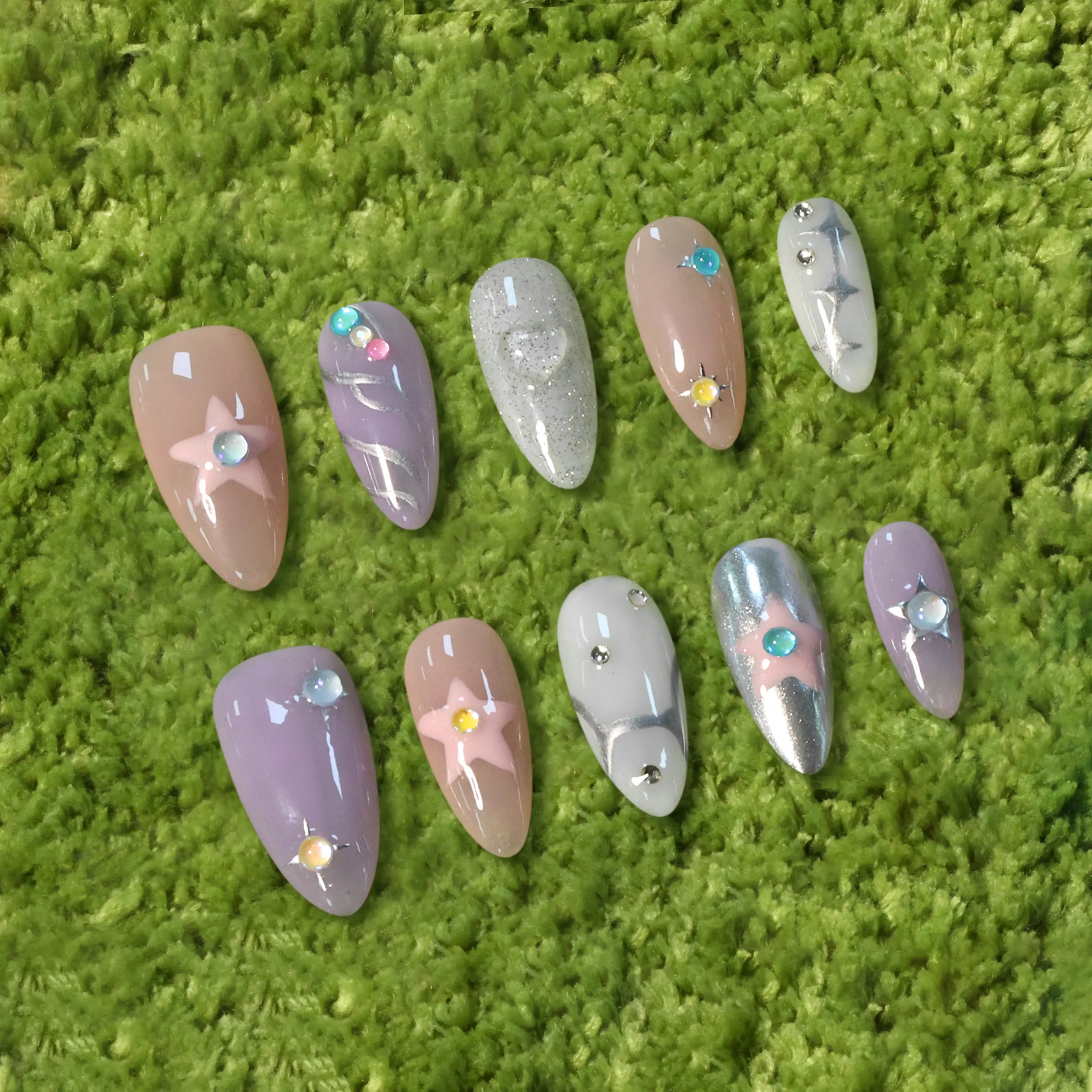 Product display showing full set of pink and lilac almond nails with pastel stars and chrome accents