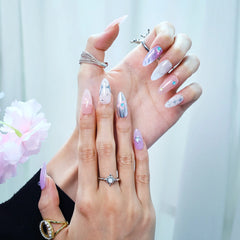 Hand model wearing almond press-on nails in pink and lilac tones with chrome shine and pastel star embellishments