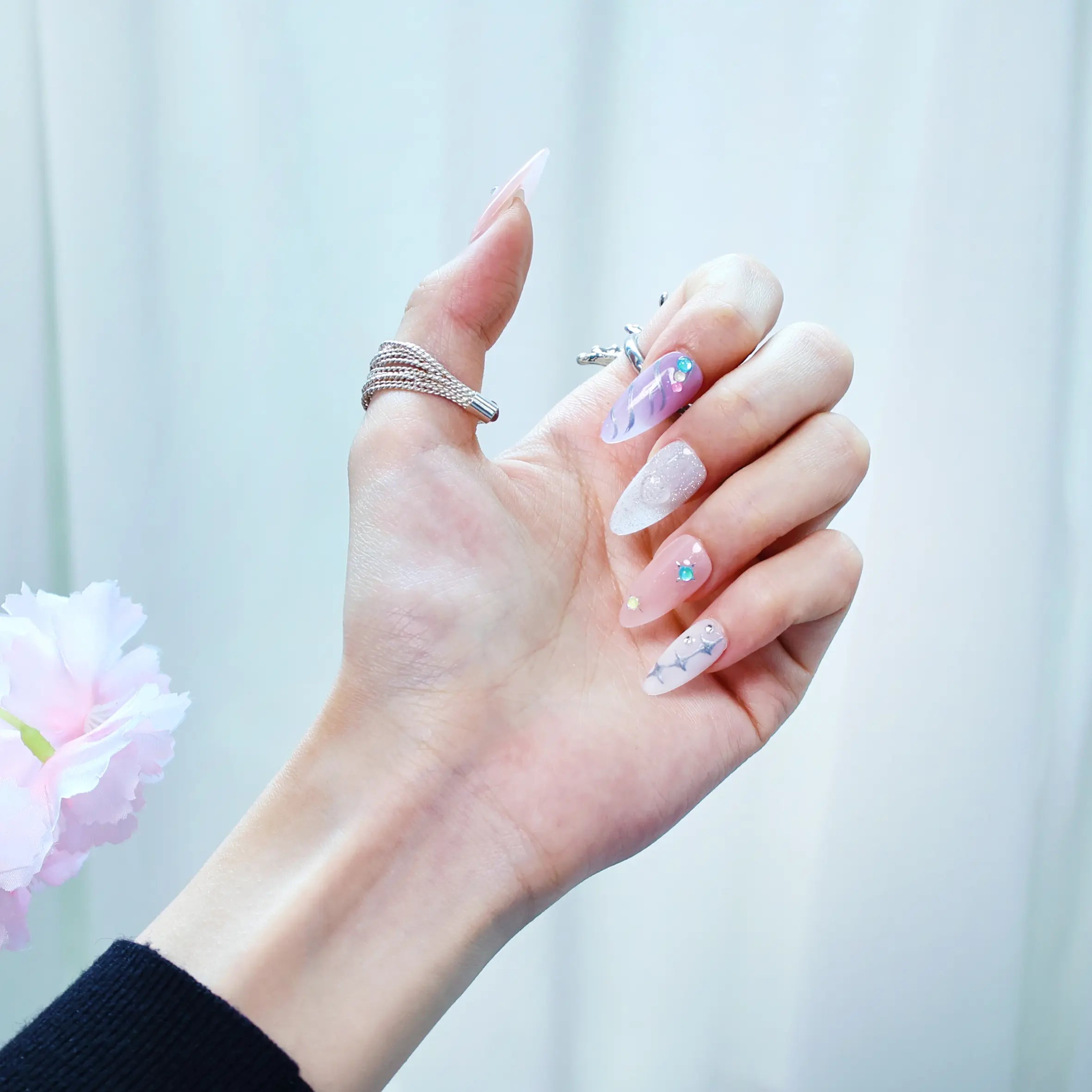 Hand pose showcasing romantic lilac and pink nails with metallic sheen and subtle fantasy elements