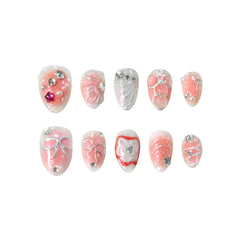 Almond-shaped pink press-on nails with 3D bows, pearls, and silver accents.