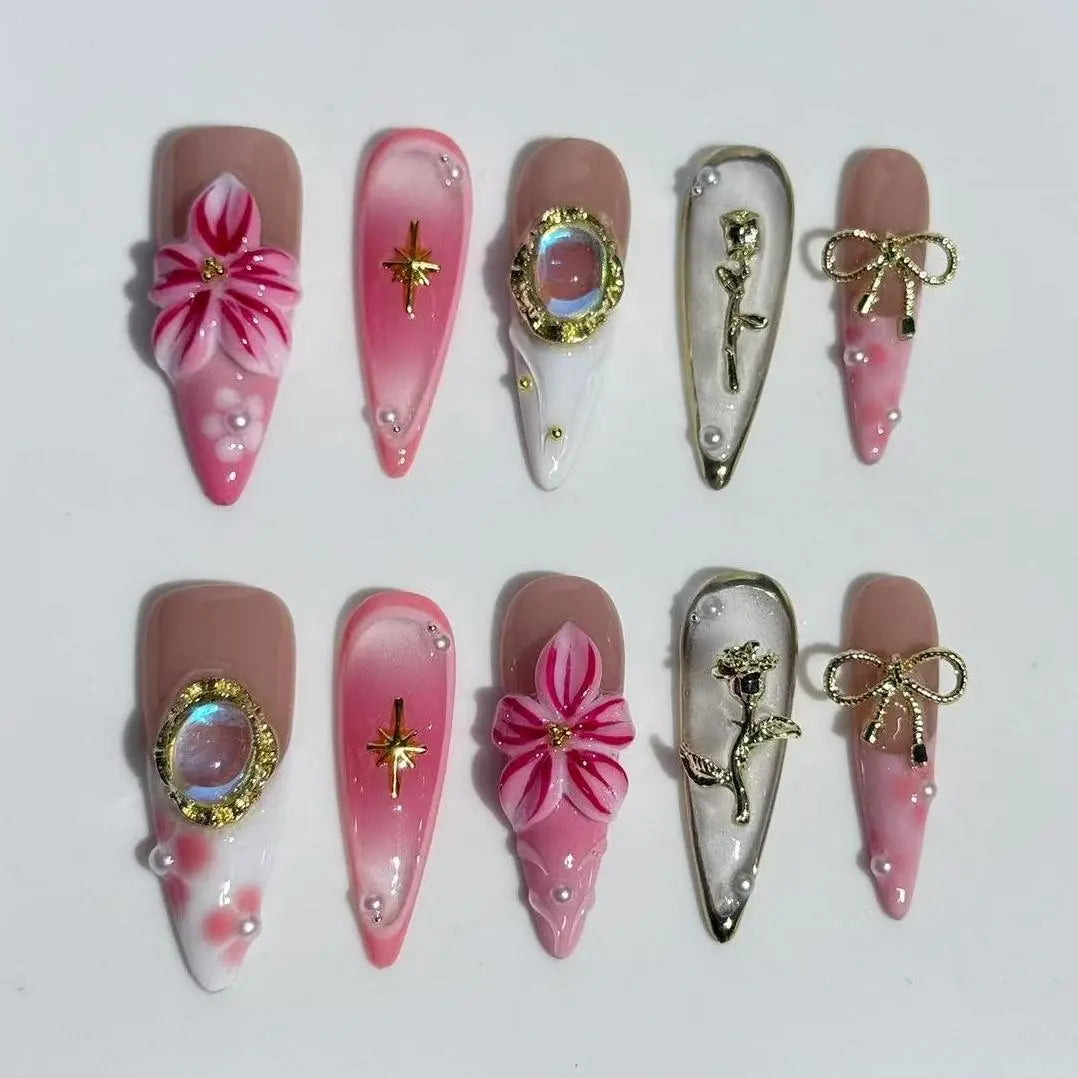 Long stiletto pink press on nails with 3D floral appliqués, rhinestones, and gold details.