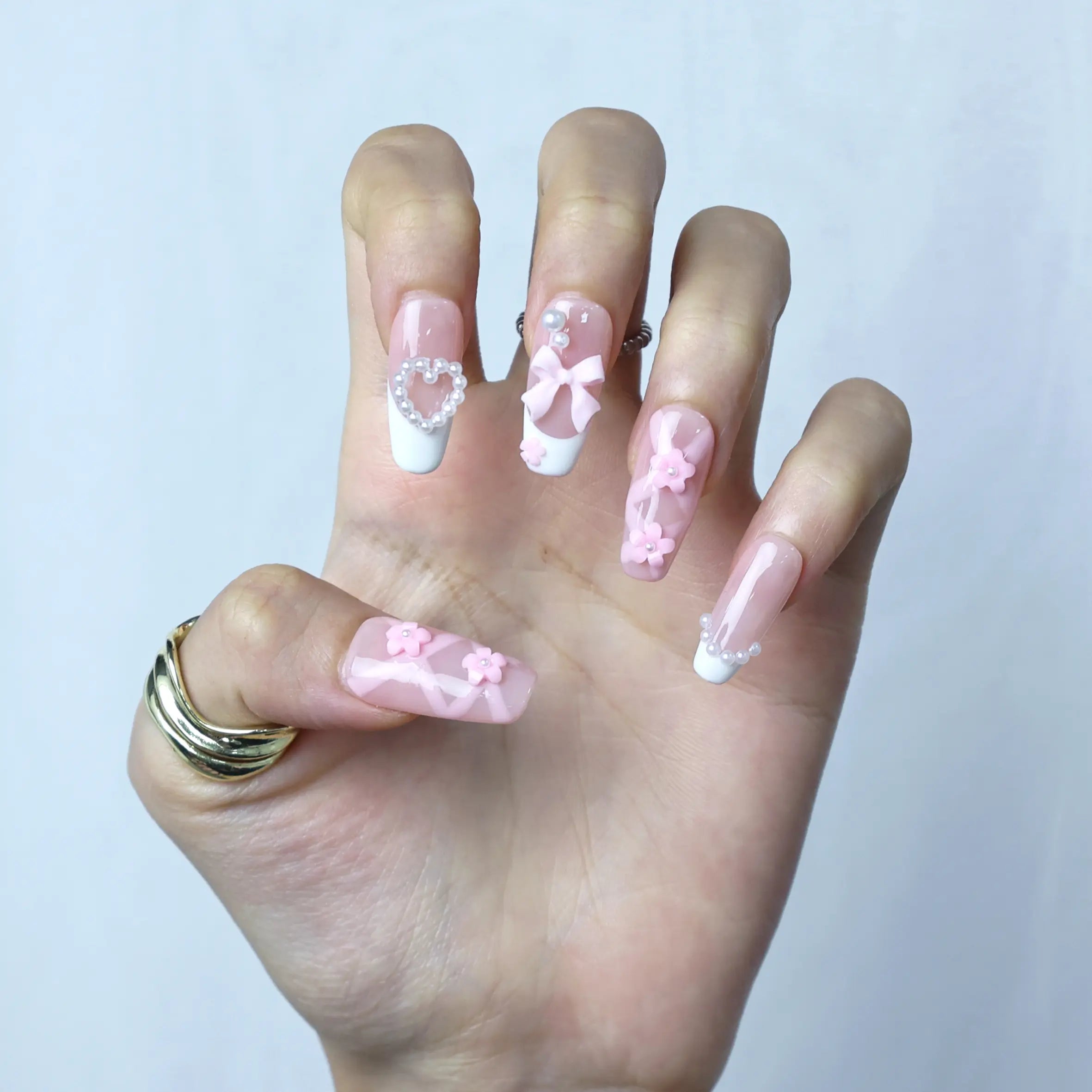 Hand model wearing pink coffin nails with sculpted white 3D flowers and delicate pearl details