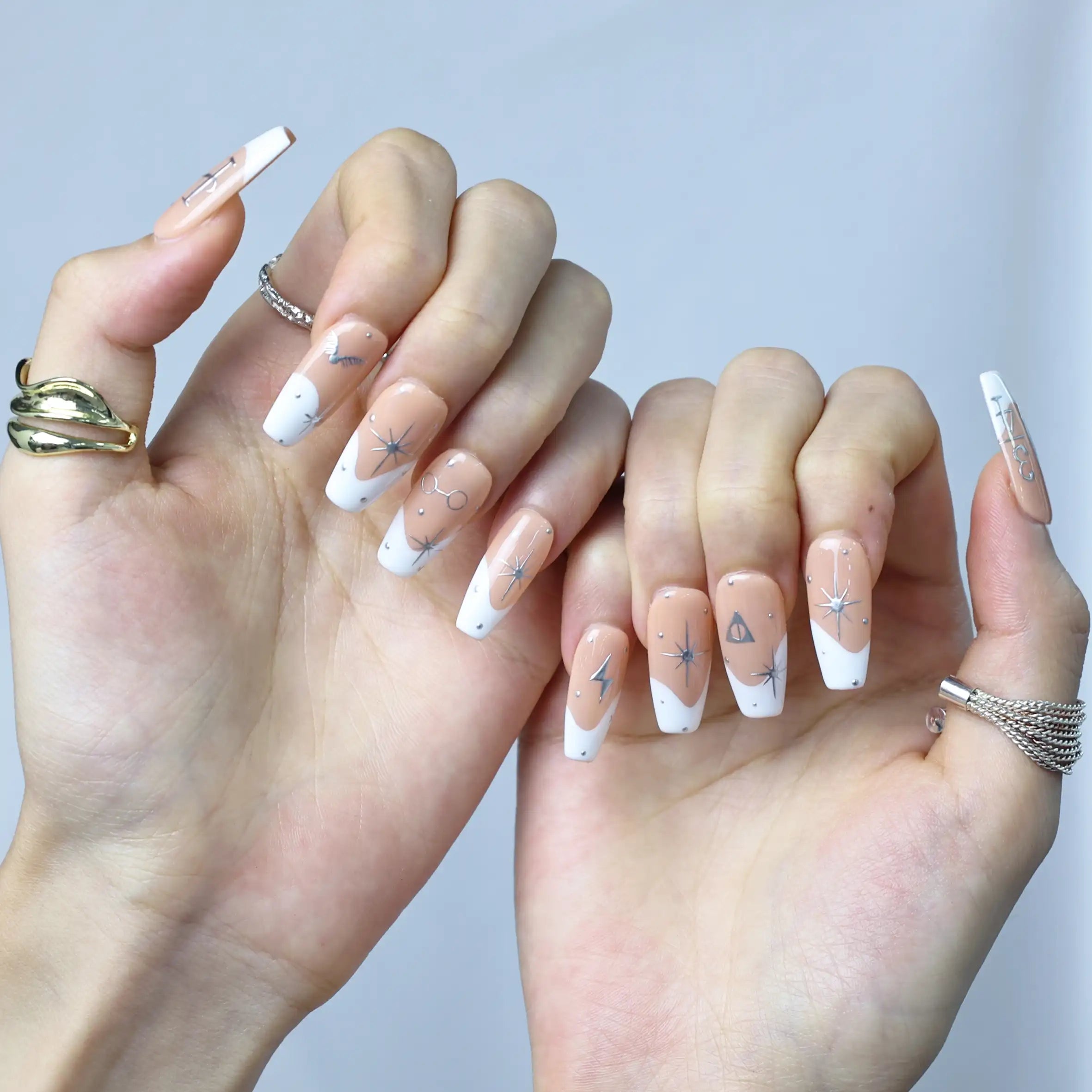 Astrology press-on nails worn with silver rings, featuring modern zodiac details on nude base