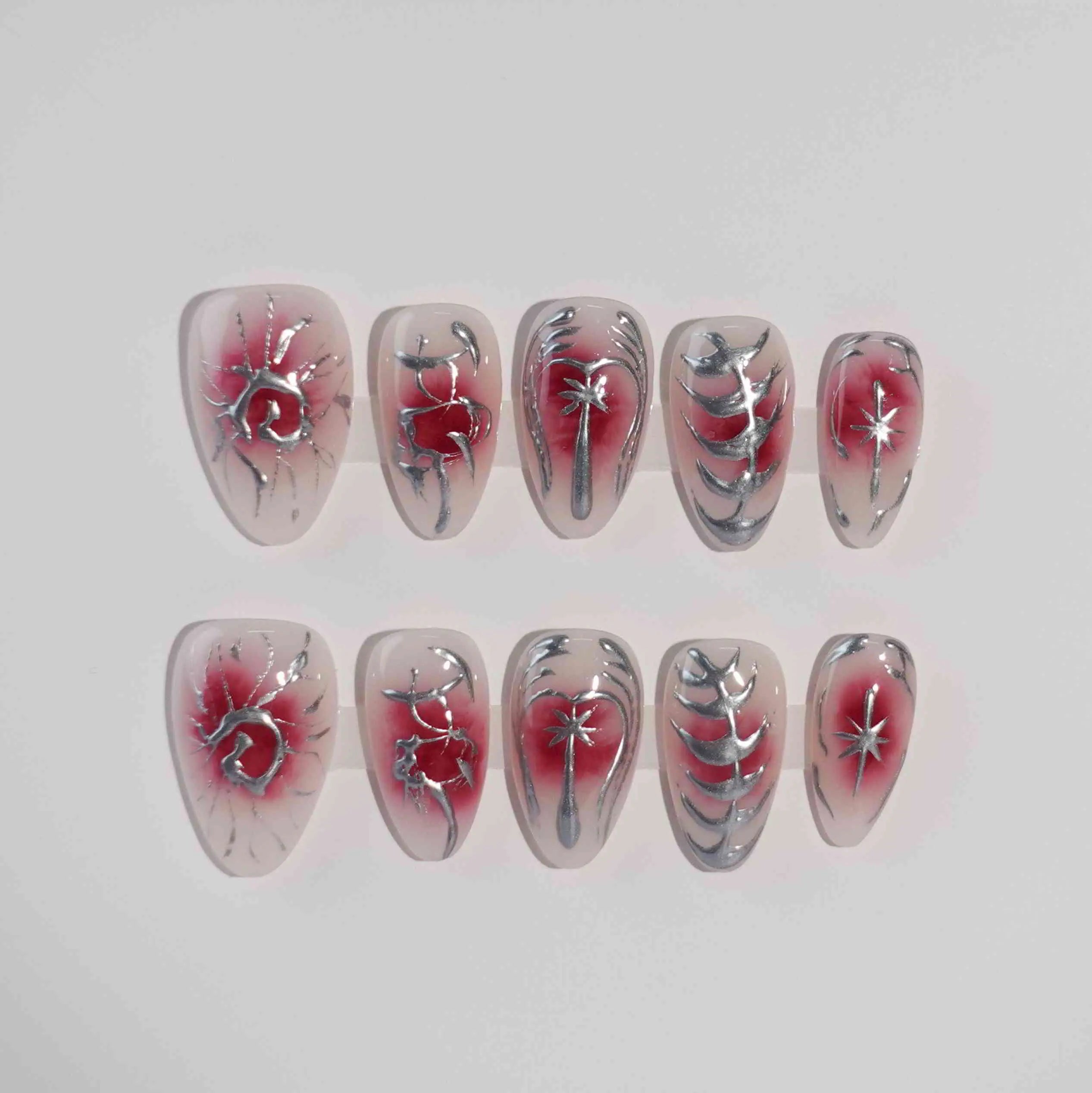 Almond-shaped red press on nails with iridescent flowers and smoky grey background.