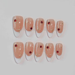 Semi-transparent red press on almond nails with scattered gemstone accents.