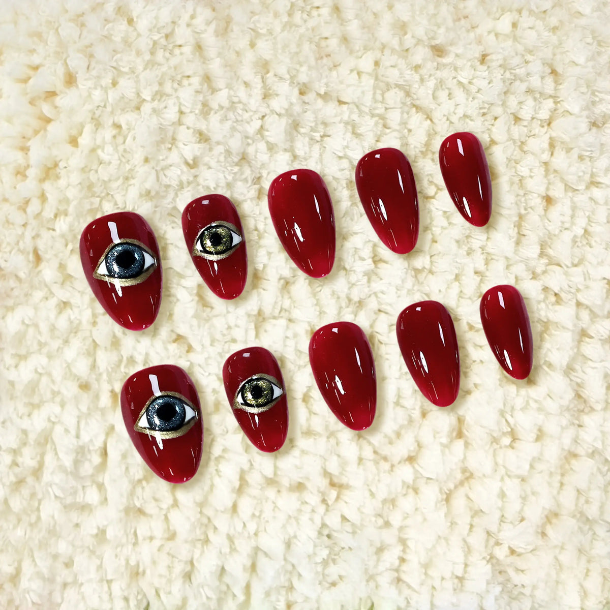 Short almond red press-on nails with glossy crimson finish, gold and black eye design for a mystical, bold aesthetic.