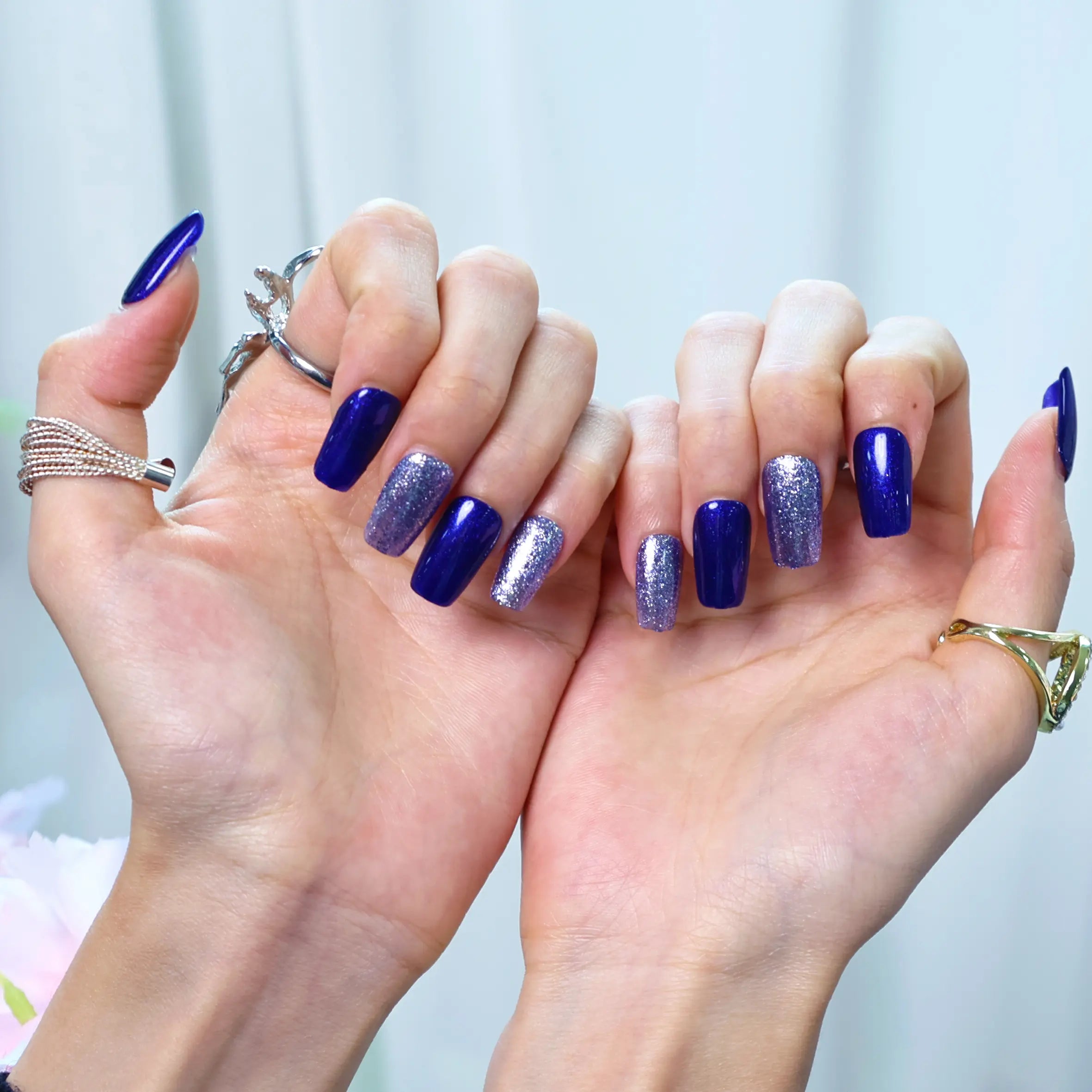 Close-up of squoval press-on nails with reflective royal blue color and glitter gradient