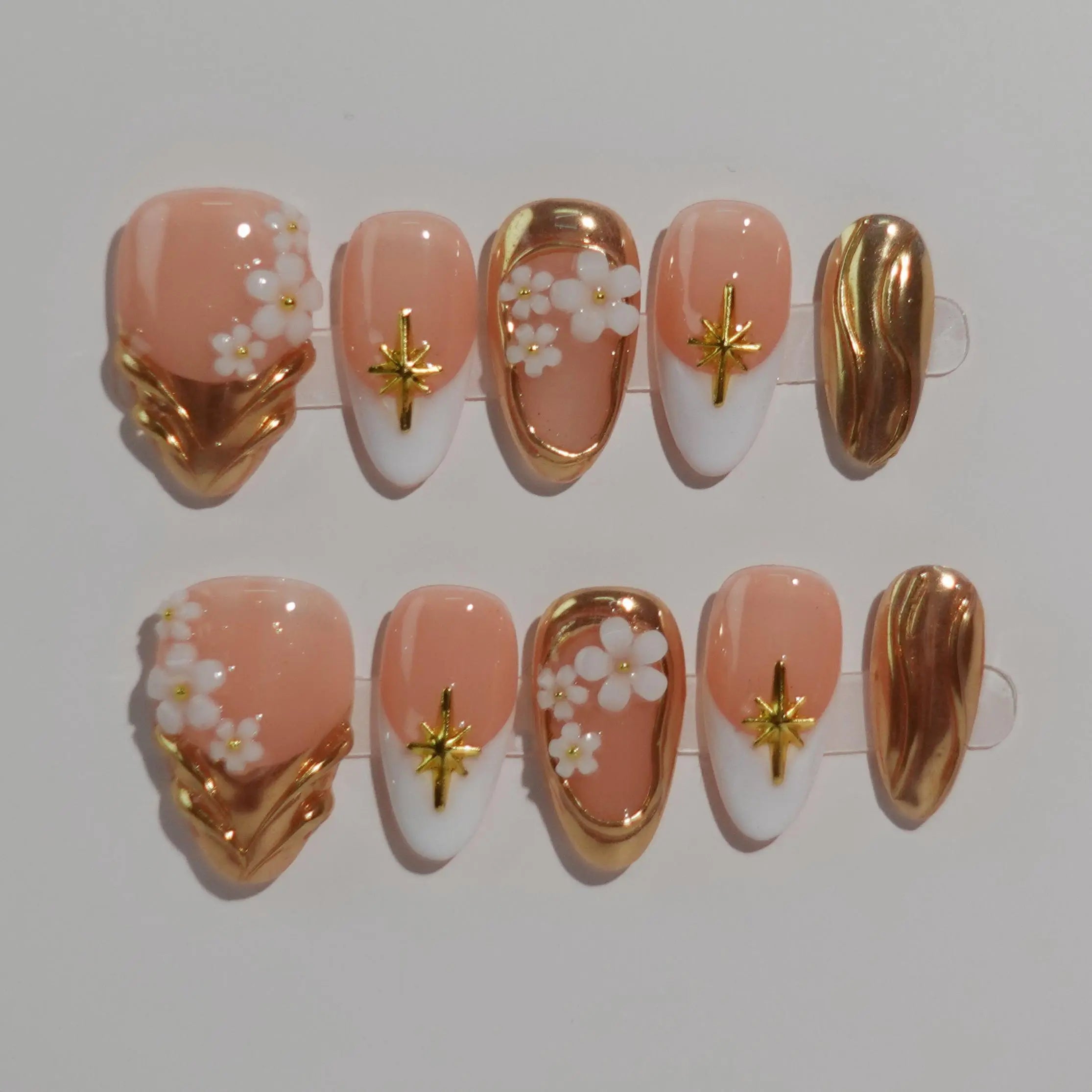 Almond press-on nails with hand-painted cherry blossoms and gold cross accents on a nude French-style base.