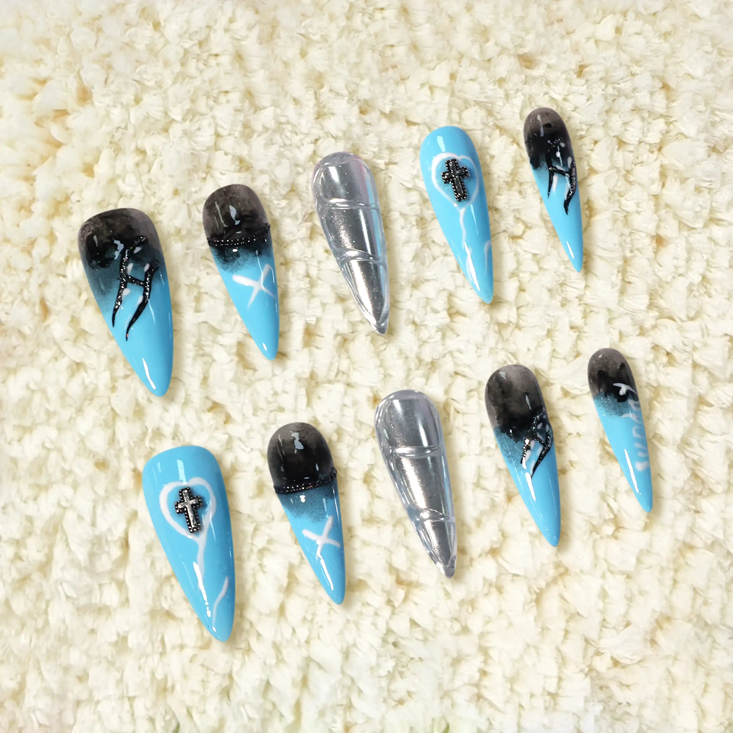 Long stiletto press-on nails with a sapphire blue to black gradient, chrome silver accents, and gothic cross charms.