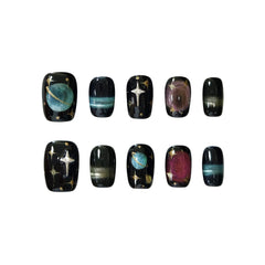 Short squoval black press-on nails with shimmering stars, metallic planets, and magnetic cat-eye auroras, inspired by the night sky