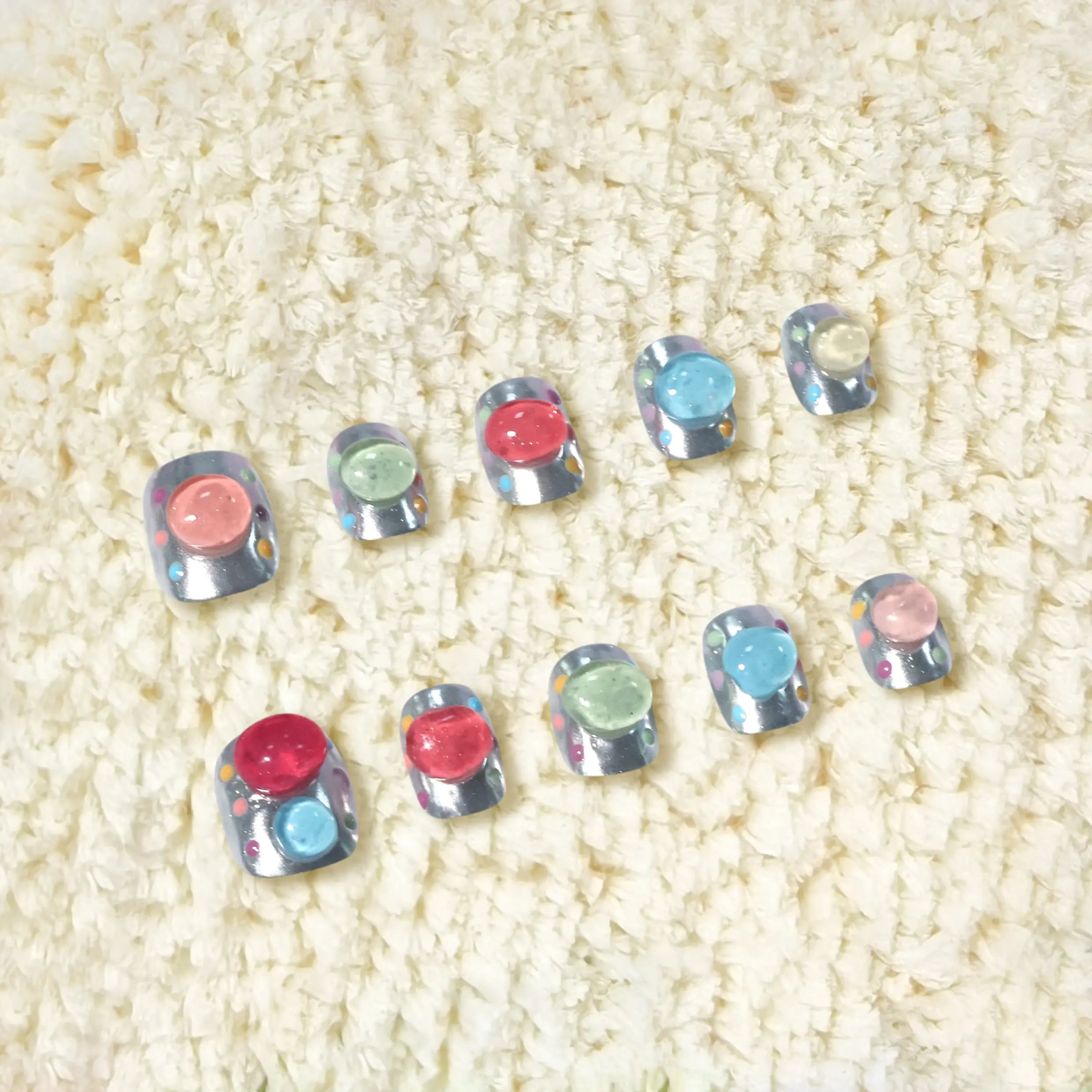 Display of full nail set with colorful jelly bubble accents on soft fabric