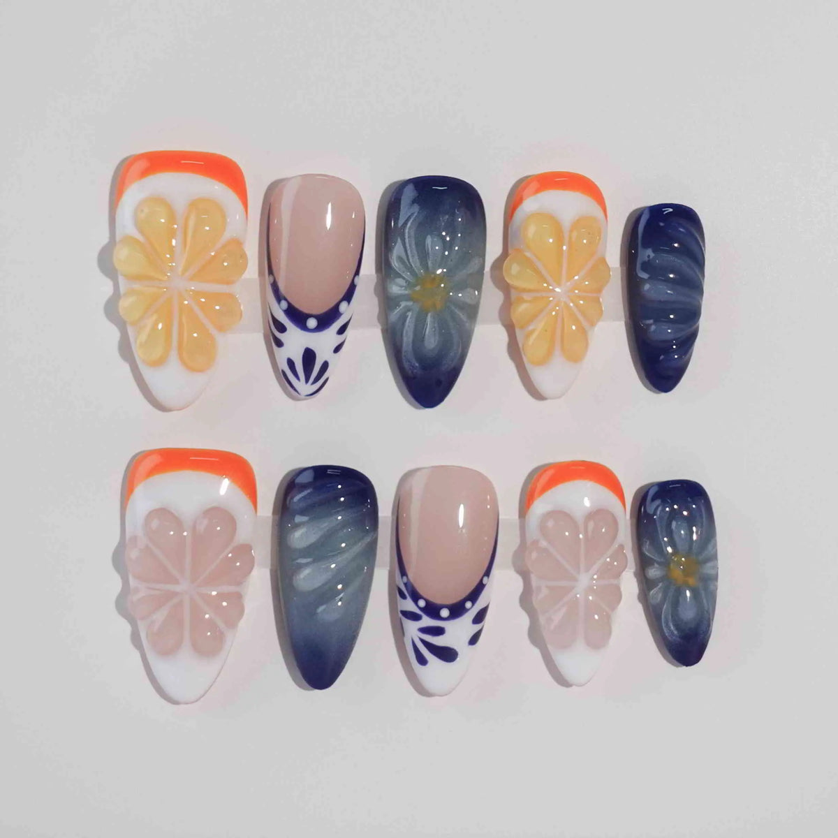 Handmade medium almond press-on nails with orange French tips, navy blue gradients, and large 3D flowers for a tropical summer look.
