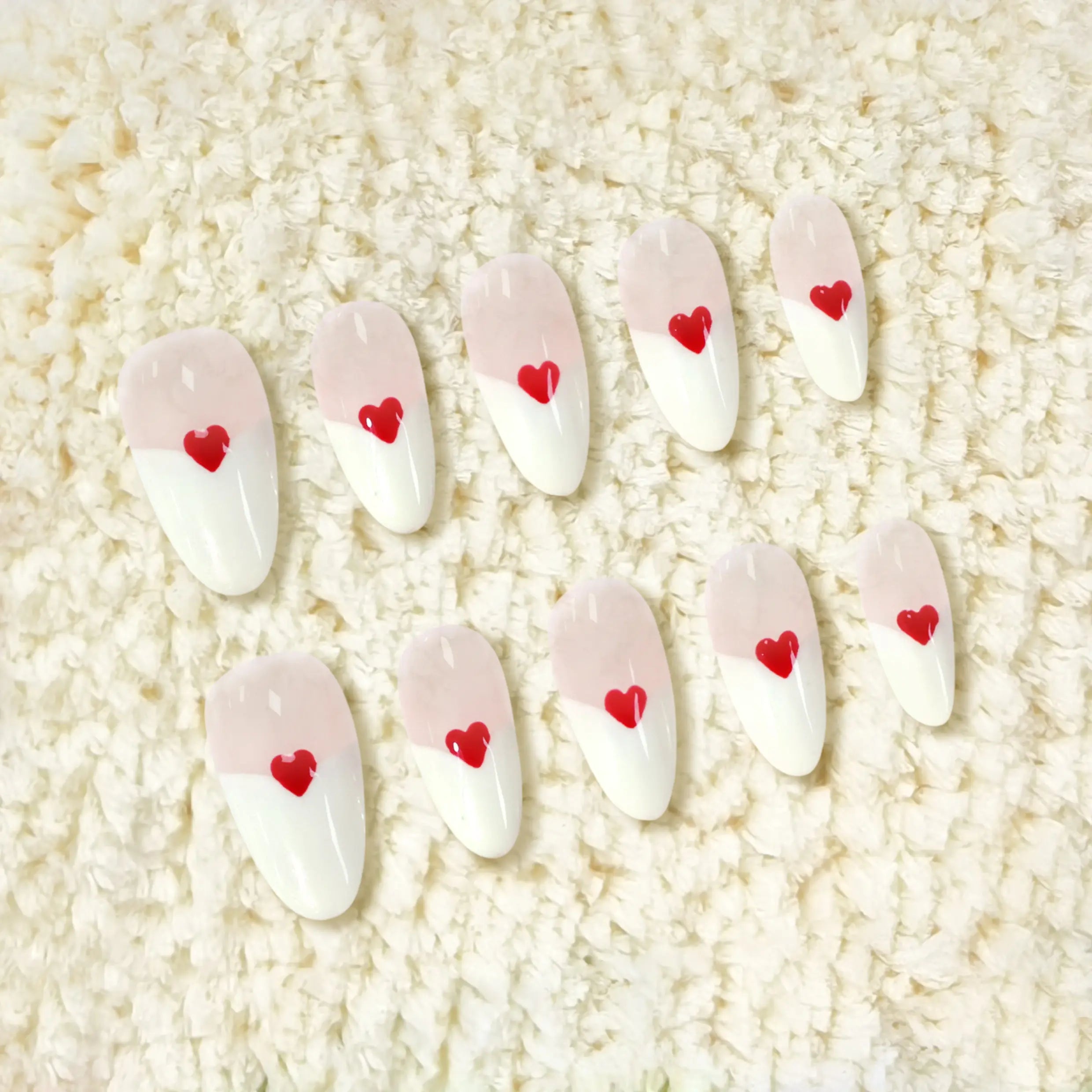 Pink almond press-on nails with red heart accents and a diagonal pink-and-white base for a romantic, feminine look.