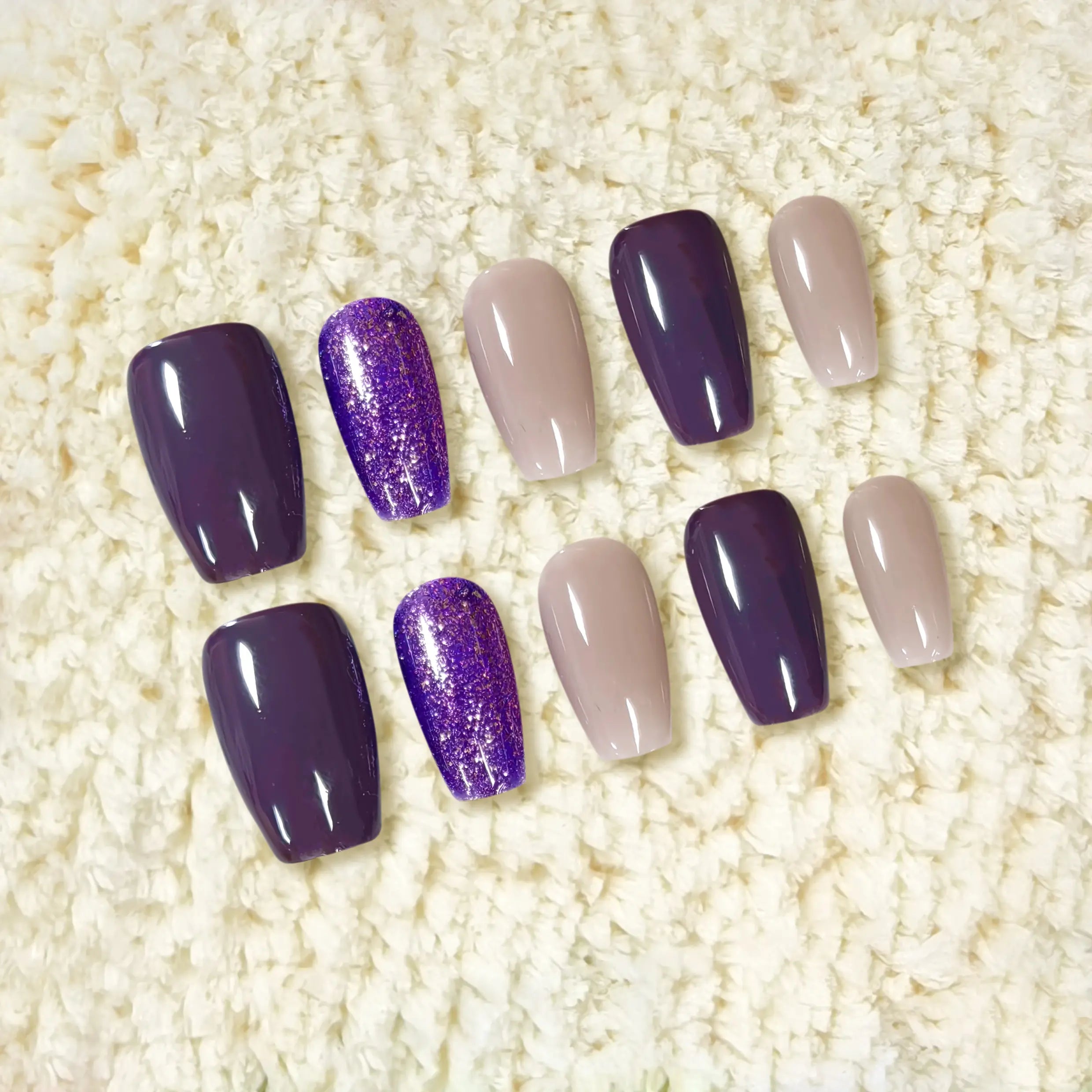 Display of full nail set with different purple tones and glitter accents