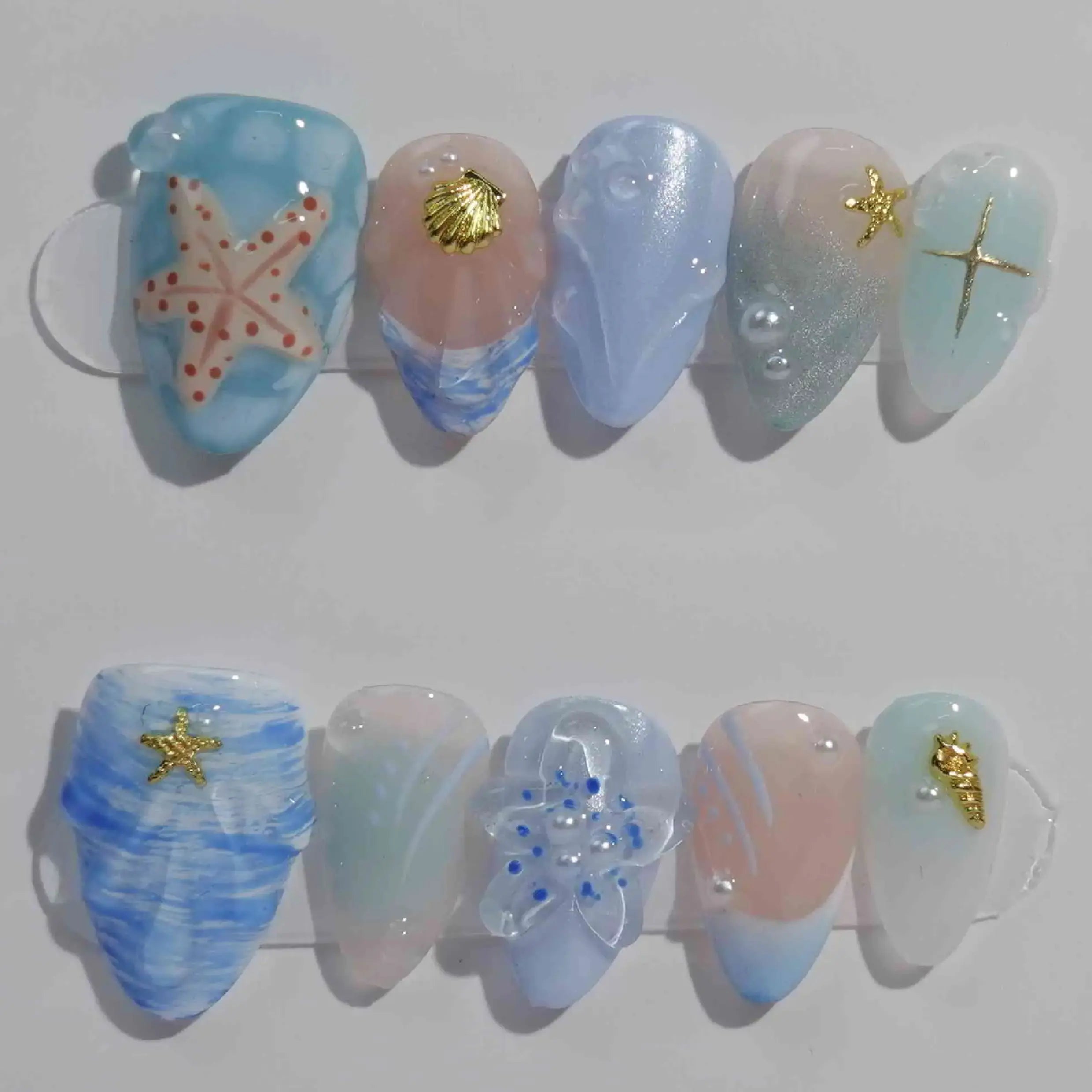 Handmade medium almond press-on nails in jellyfish blue with seashell textures and gold starfish, perfect for summer beach vibes.