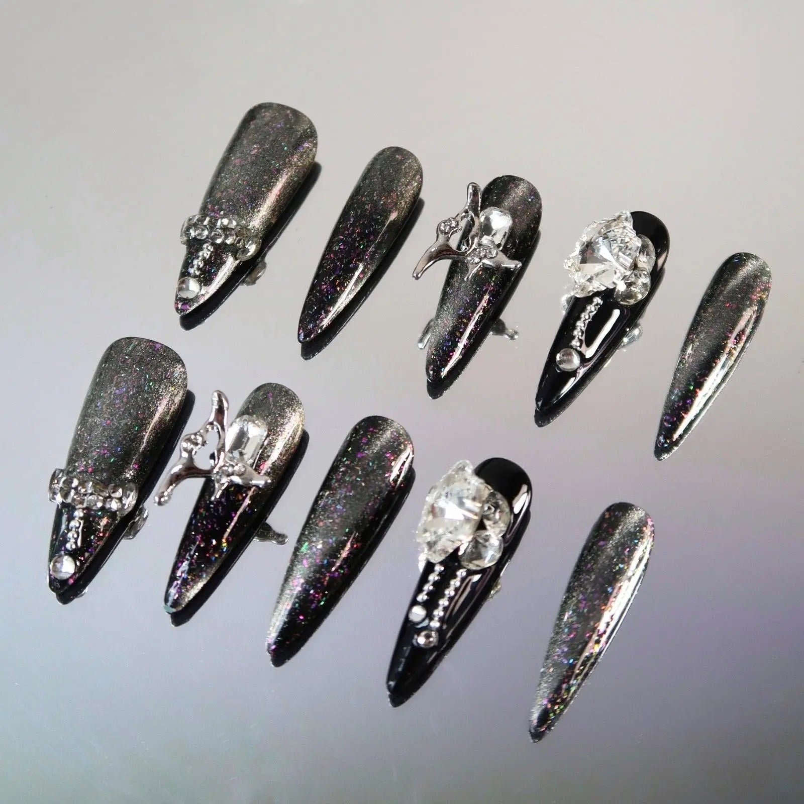 Long black stiletto press on nails with holographic chrome finish and crystal gemstone embellishments.